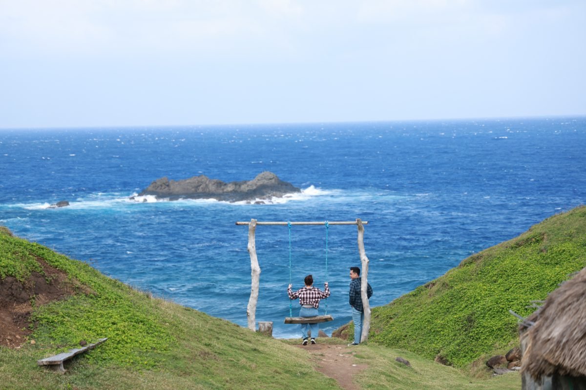Ronalyn and Karl at a rope swing on a grassy cliff above the sea